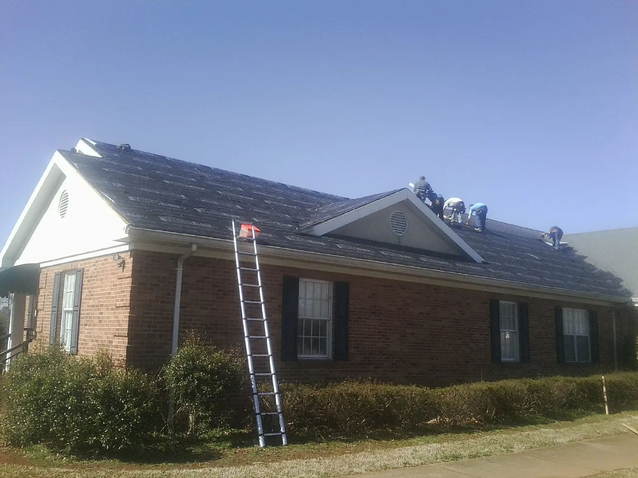 Crew tearing shingles off a brick ranch roof with a ladder set — Metal Roof Repair work by our crew in Port Republic