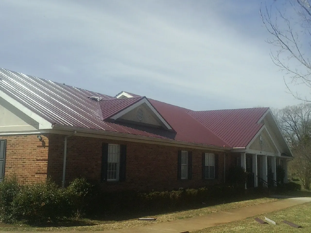 Red metal roof with gabled entries on a long brick building, from a Hail Damage Roof Repair job in Port Republic