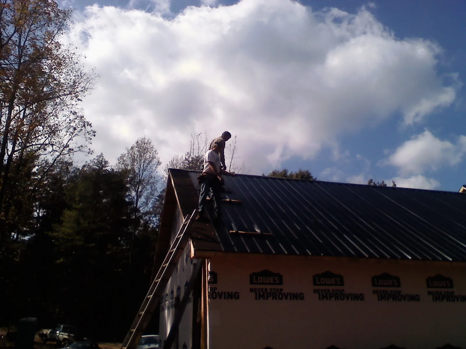 Roofer fastening dark metal panels high against a cloudy sky, from a Roof Inspection job in Port Republic